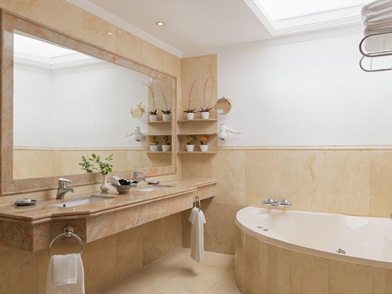 Bagno elegante con grande vasca, specchio e piastrelle beige in marmo.