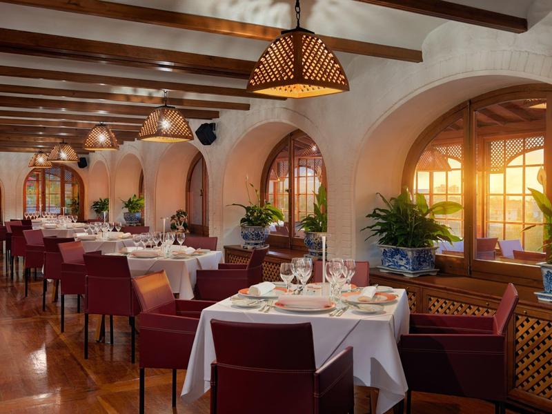 Ristorante elegante con tavoli apparecchiati e calda luce solare attraverso grandi finestre.