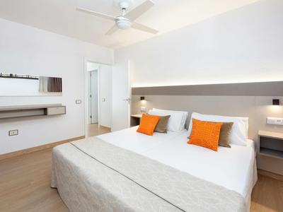 Camera luminosa e moderna con letto matrimoniale, pareti bianche e cuscini arancioni.