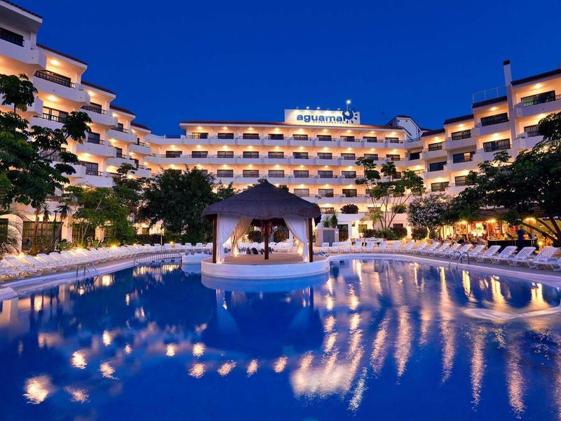 Hotel with illuminated pool and pavilion at night.