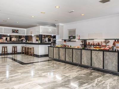 Moderne Hotel-Lobby mit hellem Marmor, langen Tresen, hohen Barhockern und weiß-grauen Wänden.