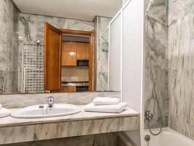 Helles Badezimmer mit Marmorwänden, Waschbecken, Handtüchern und Badewanne mit Duschvorhang.