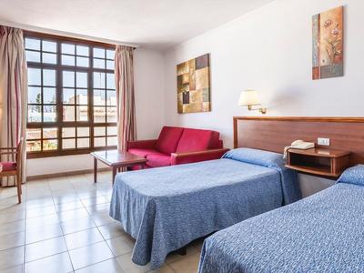 Helles Hotelzimmer mit zwei Betten, rosem Sofa, Fernseher und großem Fenster mit Gardinen.