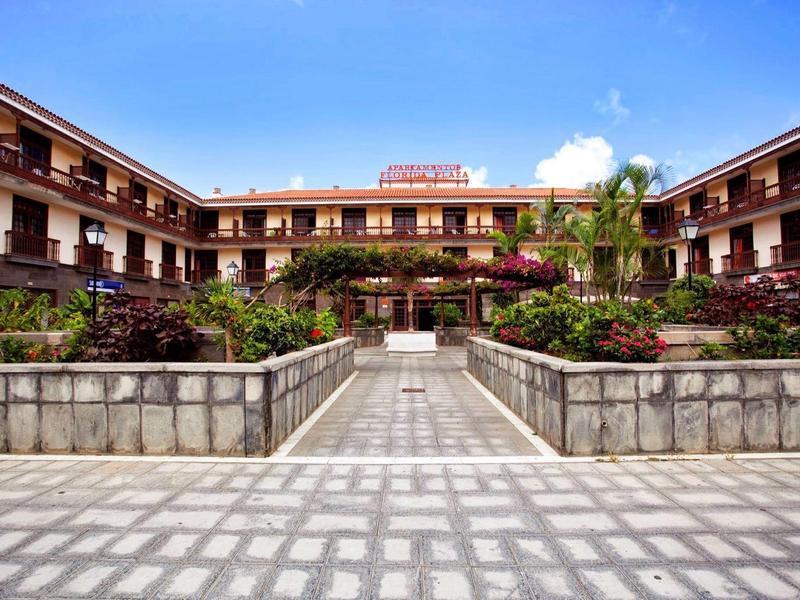 Grande hotel di tre piani con giardino e cortile lastricato sotto un cielo limpido.