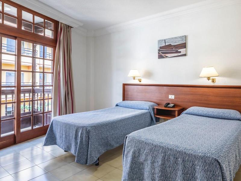 Camera d'hotel con due letti singoli, testiera in legno e grande finestra con accesso al balcone.