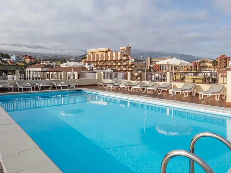 Grande piscina all'aperto con acqua azzurra limpida in un hotel con lettini e vista sugli edifici.