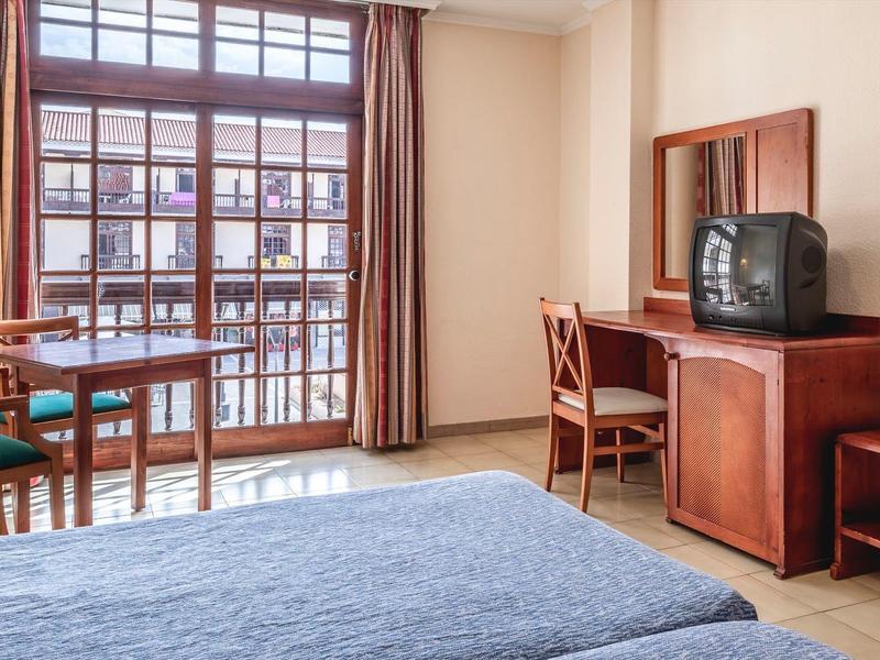 Camera d'hotel con letto matrimoniale, tavolo, sedie, TV e grande finestra con vista sul balcone.