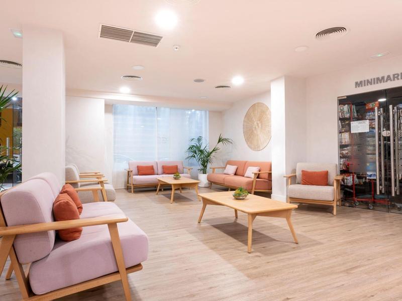 Zona lounge luminosa e moderna con divani, tavoli e minimarket.