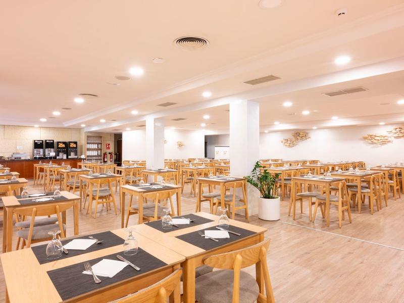 Ampia sala colazione con tavoli e sedie in legno apparecchiati con tovagliette nere e posate.