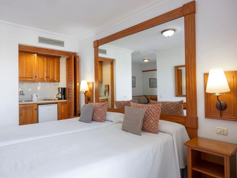 Camera d'hotel con due letti singoli, grande specchio a parete e angolo cottura sullo sfondo.