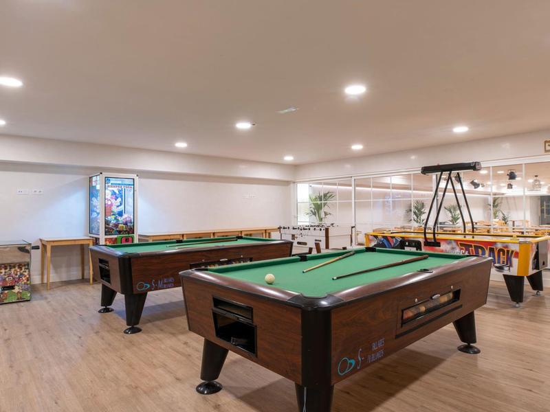 Una grande sala giochi luminosa con tavoli da biliardo, un calcio balilla e un distributore automatico.