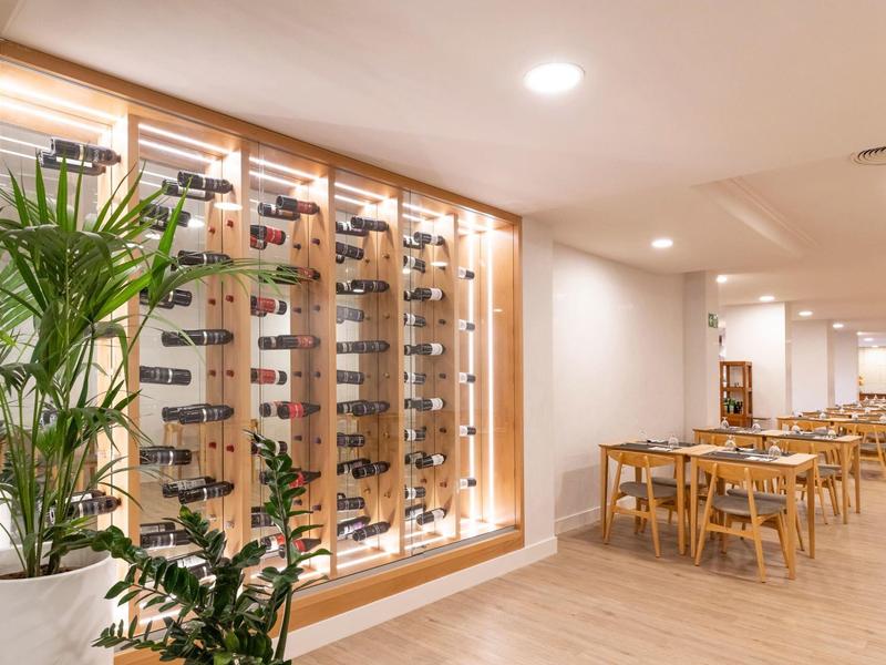 Ristorante moderno con porta bicchieri da vino, piante e tavoli in legno in un'atmosfera luminosa e accogliente.