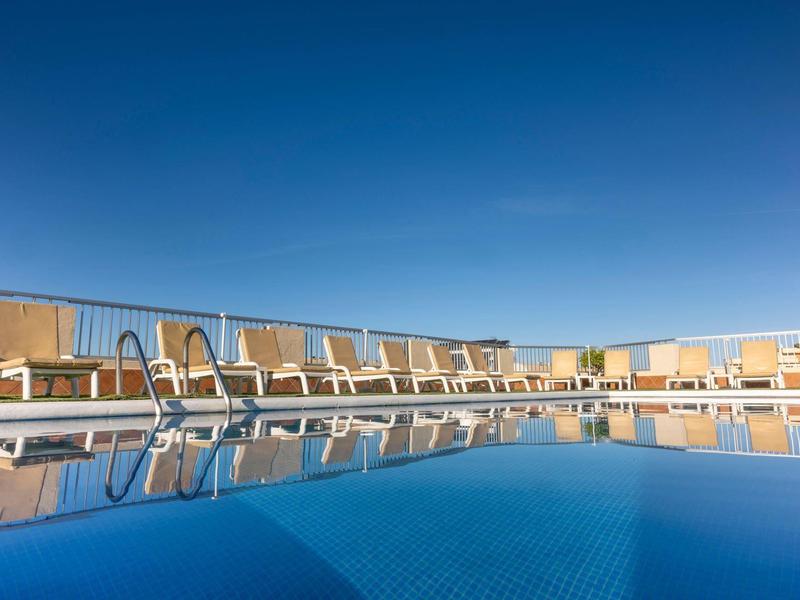 Piscina limpida con più lettini sotto un cielo azzurro su una terrazza dell'hotel.