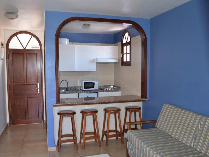Small kitchen with counter and four stools, next to a striped sofa in a blue room.