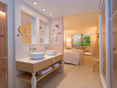 Helles Badezimmer mit doppeltem Waschbecken und angrenzendem Schlafzimmer mit großem Fenster.