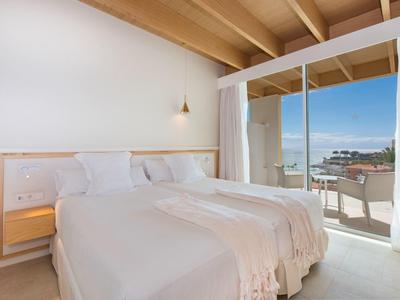 Helles Schlafzimmer mit Holzdecke, großem Bett, Balkon und Meerblick durch Glastür.