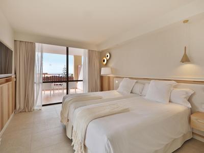 Helles Hotelzimmer mit zwei Betten, Holzmo?beln, Balkon und beigeweißen Wänden.