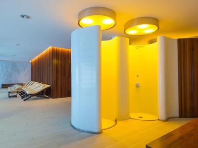 Moderner Wellnessbereich mit runden Duschen, warmem Licht und Liegestühlen im Hintergrund.