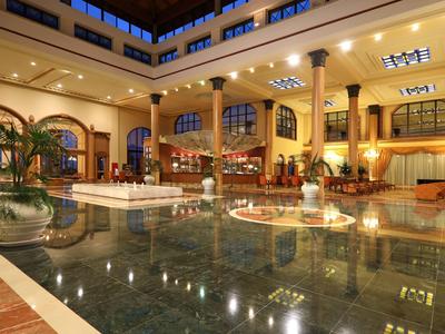 Großer Innenpool mit Marmorfliesen, Palmen und elegantem, warm beleuchtetem Lobbybereich.