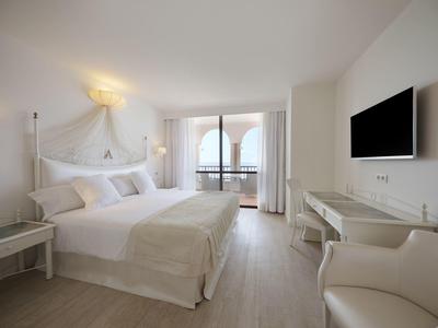 Helles Schlafzimmer mit großem Bett, weißer Einrichtung, Balkon und Flachbildschirm an der Wand.