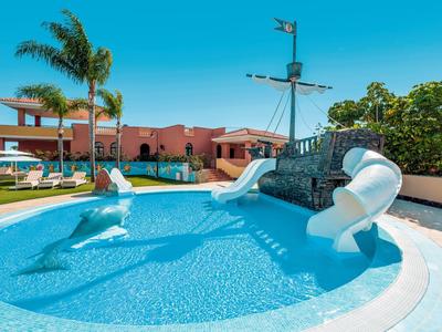 Pool mit rutschbahn in form eines schiffs, umgeben von pflanzen und einem mehrstöckigen gebäude.