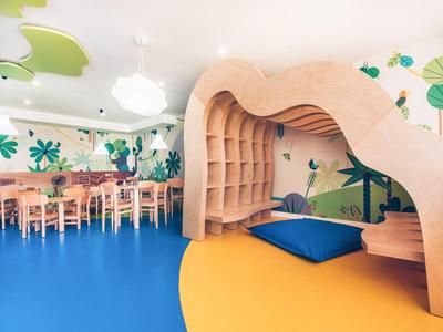 Kinderzimmer mit buntem Boden, Waldbild an Wand, Tischen, Stühlen und organischem Holzregal.