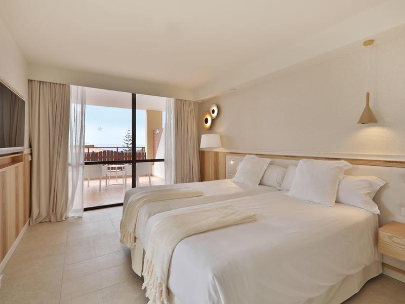 Helles Hotelzimmer mit zwei Betten, Holzmo?beln, Balkon und beigeweißen Wänden.