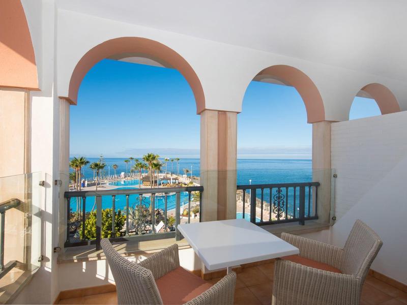 Terrasse mit weißen Säulen, Meerblick, blauem Himmel und Möbeln aus Rattan in hellem Beige.