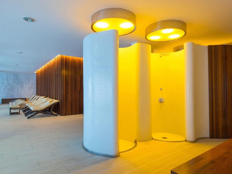 Moderner Wellnessbereich mit runden Duschen, warmem Licht und Liegestühlen im Hintergrund.