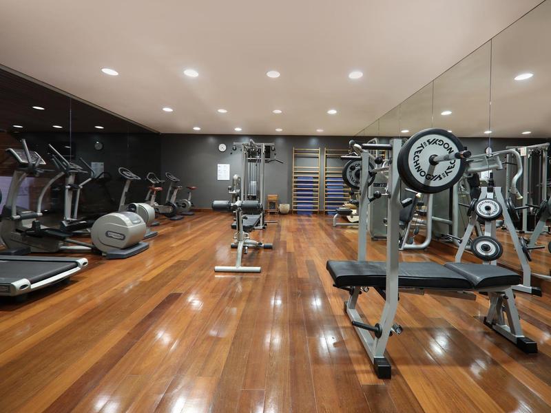 Moderner Fitnessraum mit Holzboden, Spiegelwand und verschiedenen Trainingsgeräten wie Laufbändern und Gewichten.
