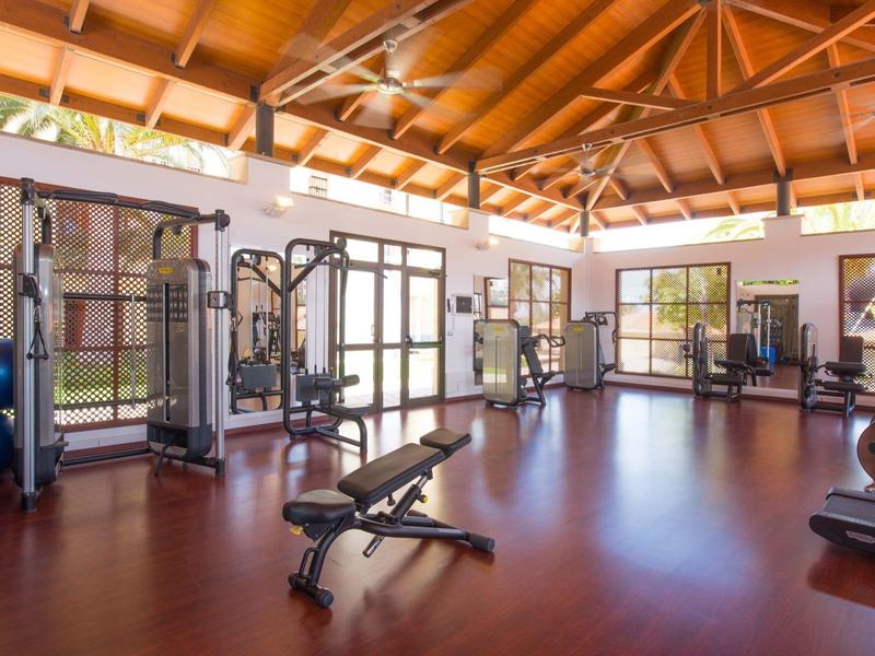 Heller Fitnessraum mit Holzboden, Holzdach, Trainingsgeräten und großen Fenstern.