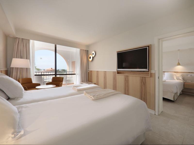 Modern eingerichtetes Schlafzimmer mit Doppelbett, Fernseher und Zugang zum angrenzenden Zimmer.