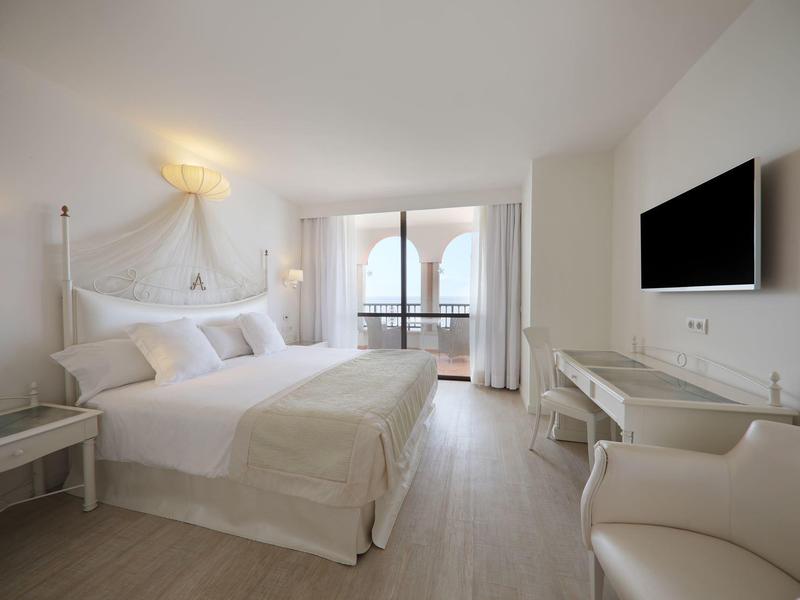 Helles Schlafzimmer mit großem Bett, weißer Einrichtung, Balkon und Flachbildschirm an der Wand.