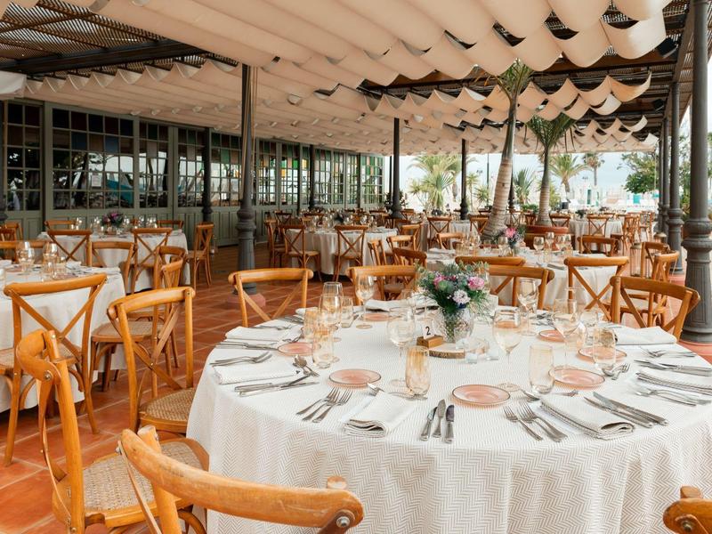 Freiluft-Restaurant mit weißen Tischdecken, Holzmöbeln und gedeckten Tischen unter Sonnendach.