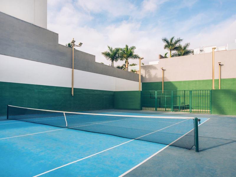 Leerer Tennisplatz mit blauem Boden, grün-weißen Wänden und Palmen im Hintergrund.