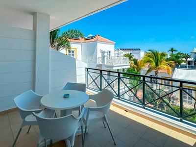 Balcony with table and four chairs, overlooking a palm-lined residential area in sunny weather.