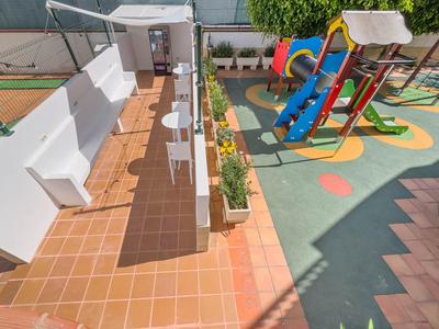 Ein sonniger Außenbereich mit Sitzgelegenheiten und einem farbenfrohen Kinderspielplatz.