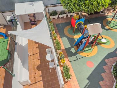 Ein moderner Spielplatz mit bunten Geräten und Sitzbereichen im Freien neben einem Hotelgebäude.