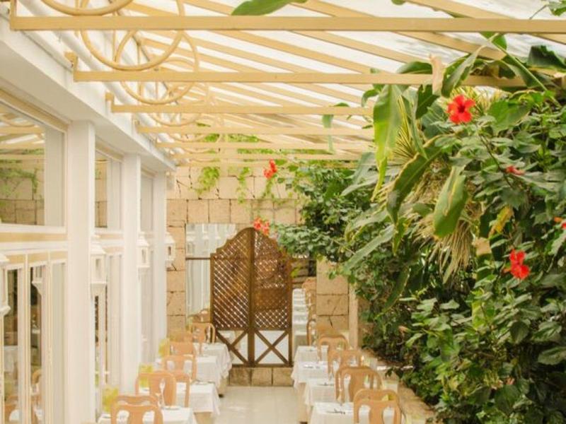 Brightly lit balcony with white chairs and lush green wall in a hotel area.