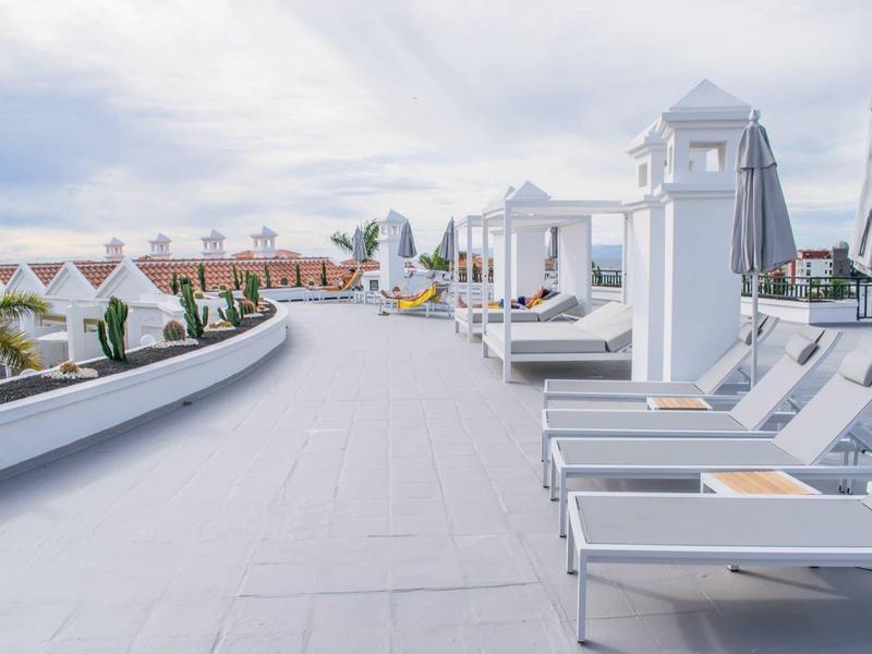 Modern loungers with umbrellas at a hotel pool area overlooking buildings.