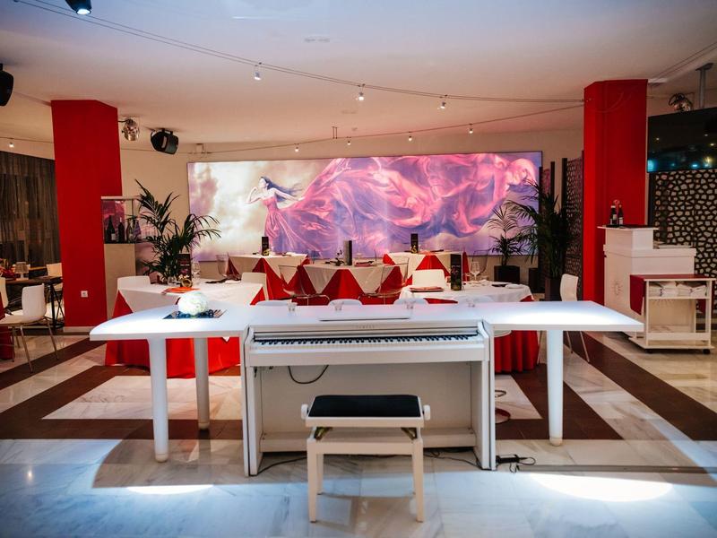 Modern white grand piano in a stylish hotel lobby area with red accents and seating.