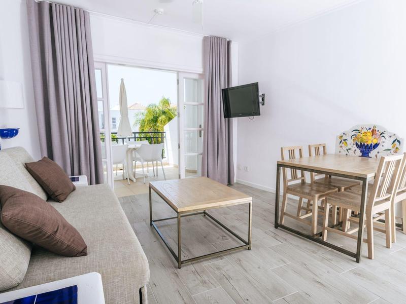 Modern living room with sofa, coffee table, dining table, and balcony overlooking greenery.