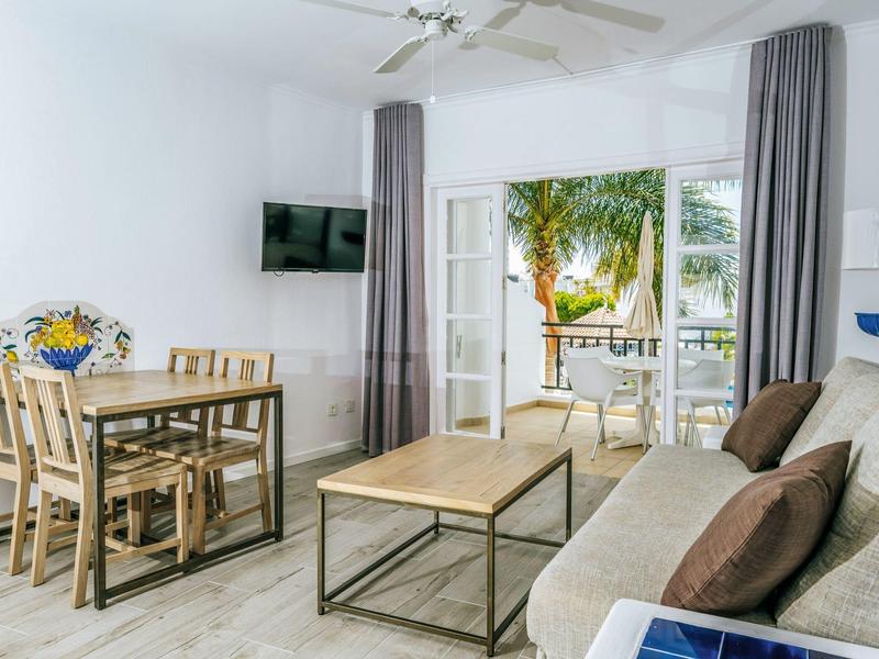 Bright living room with dining table, sofa, and view of a terrace with palm trees.
