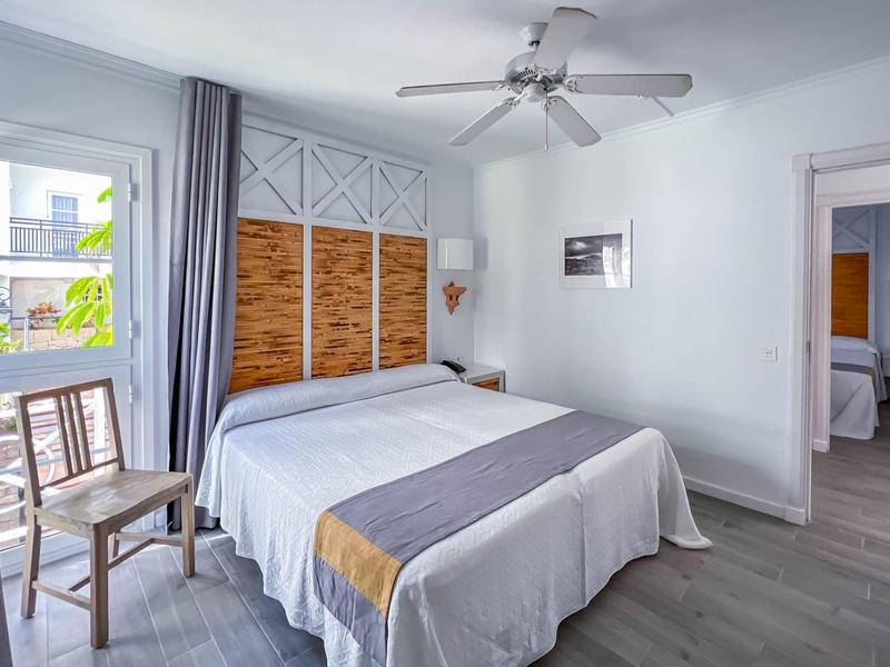 Bright hotel room with double bed, wooden chair, ceiling fan, and modern design.