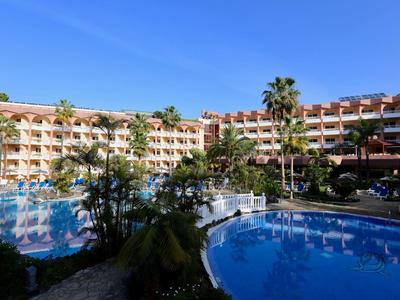 Hotel mit großem Pool und Palmen unter klarem blauem Himmel.
