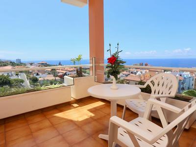 Balkon mit Tisch, Stühlen und Blumen mit Blick auf das Meer und die Stadt unter blauem Himmel.