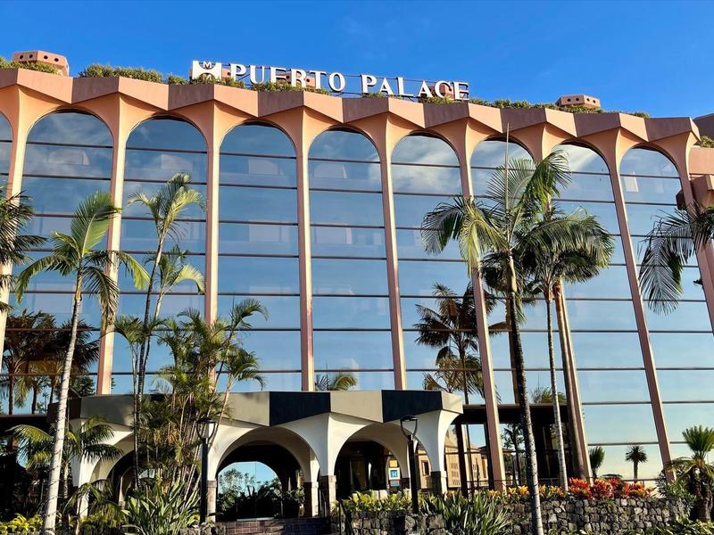 Edificio alberghiero moderno con facciata in vetro e palme sotto un cielo azzurro