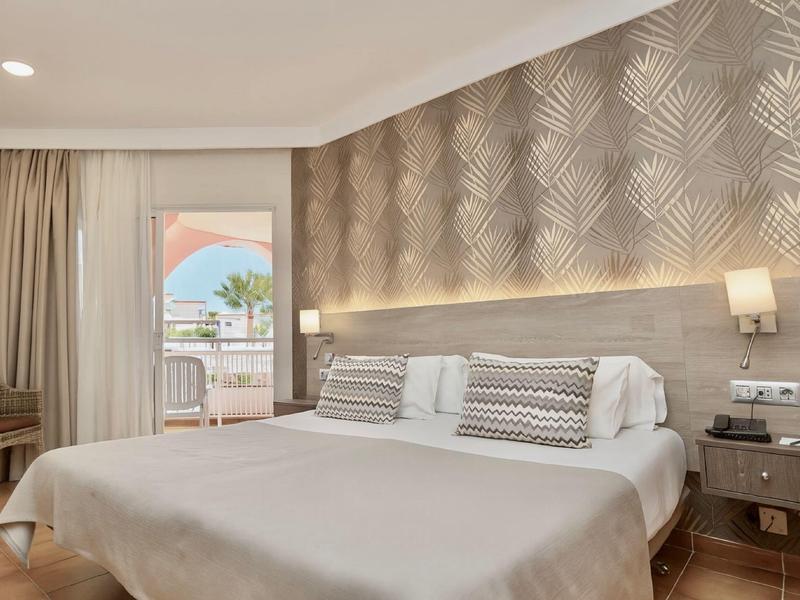 Camera d'hotel moderna con letto matrimoniale, lampade e balcone con vista sulla piscina.