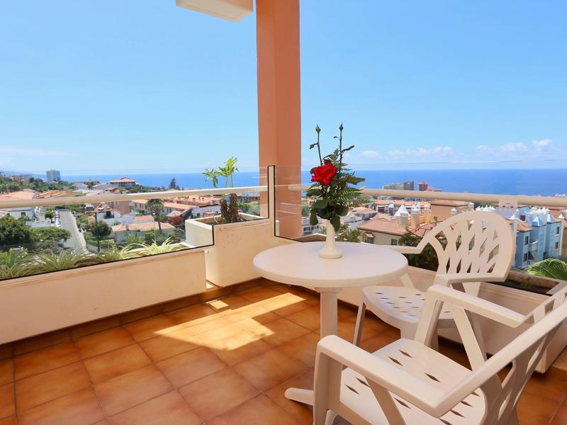 Balcone con sedie di plastica e tavolo con vista sul mare e sulla città sotto un cielo azzurro.