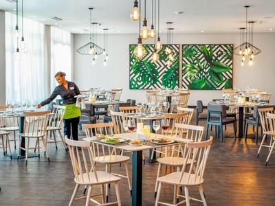 Prázdná restaurace s dřevěnými stoly a židlemi, dekorovaná zelenými nástěnnými obrazy